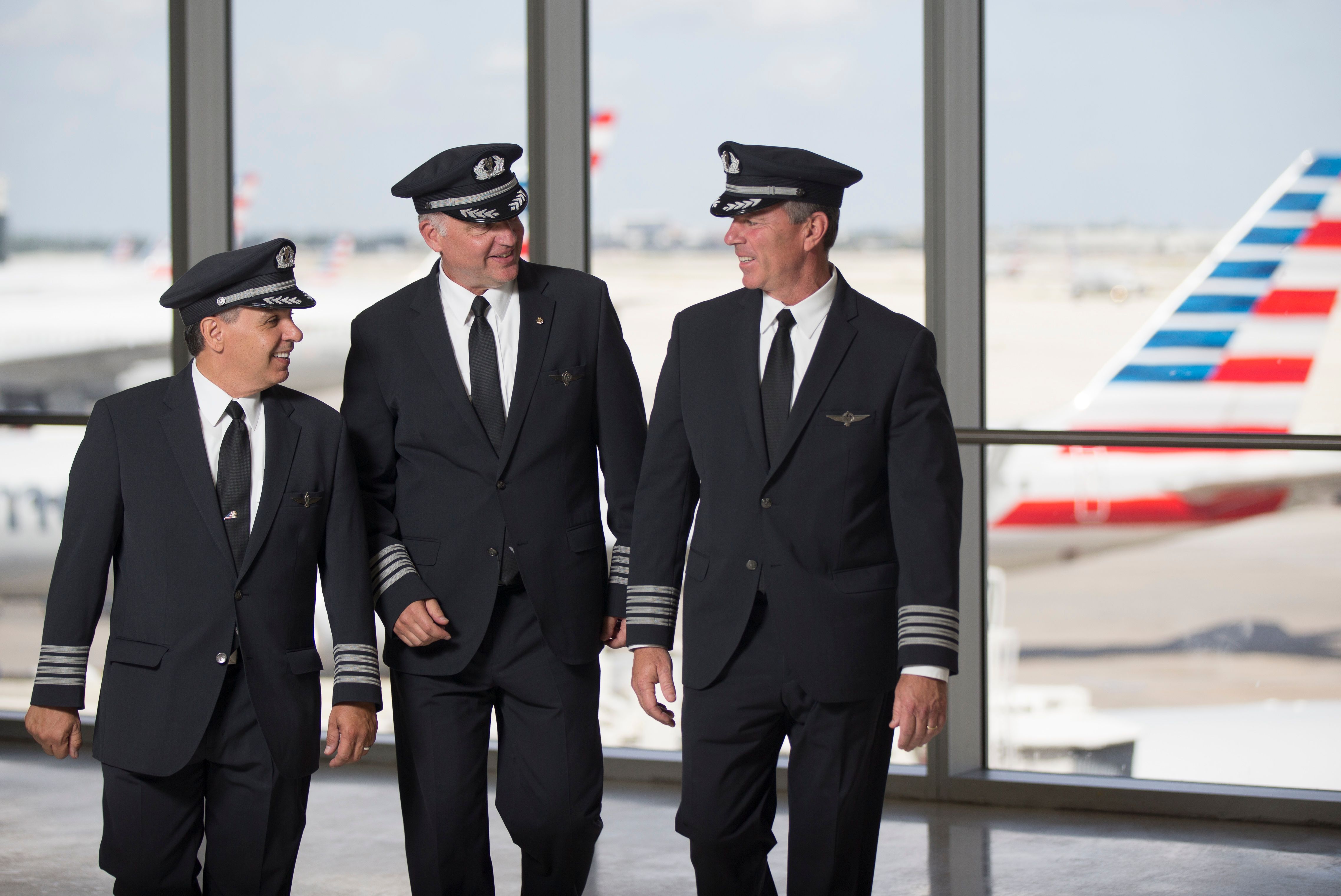 Three captains conversing at an airport gate.