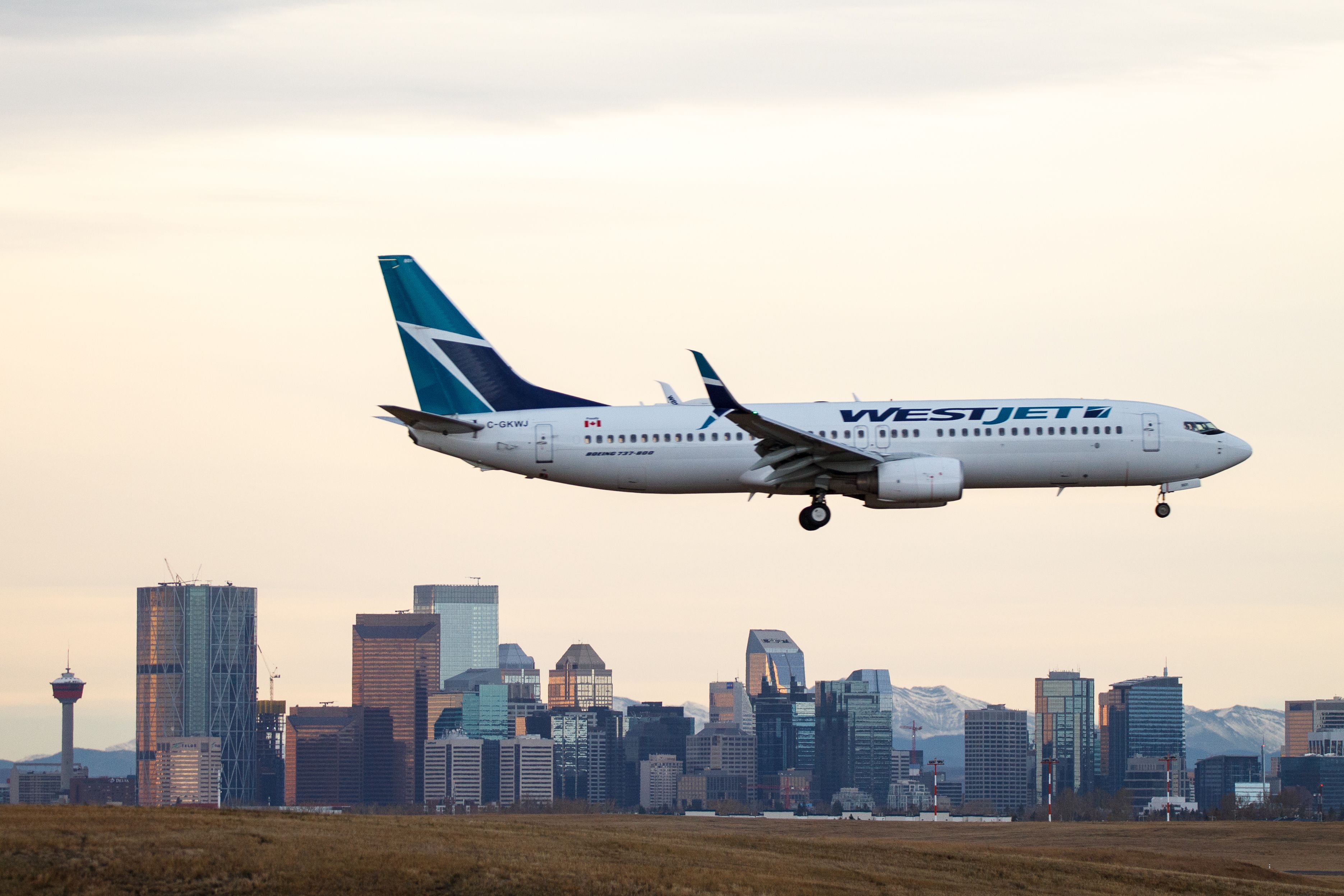WestJet Airlines C-GKWJ Boeing 737-800 landing over the city skyline at Calgary International Airport.