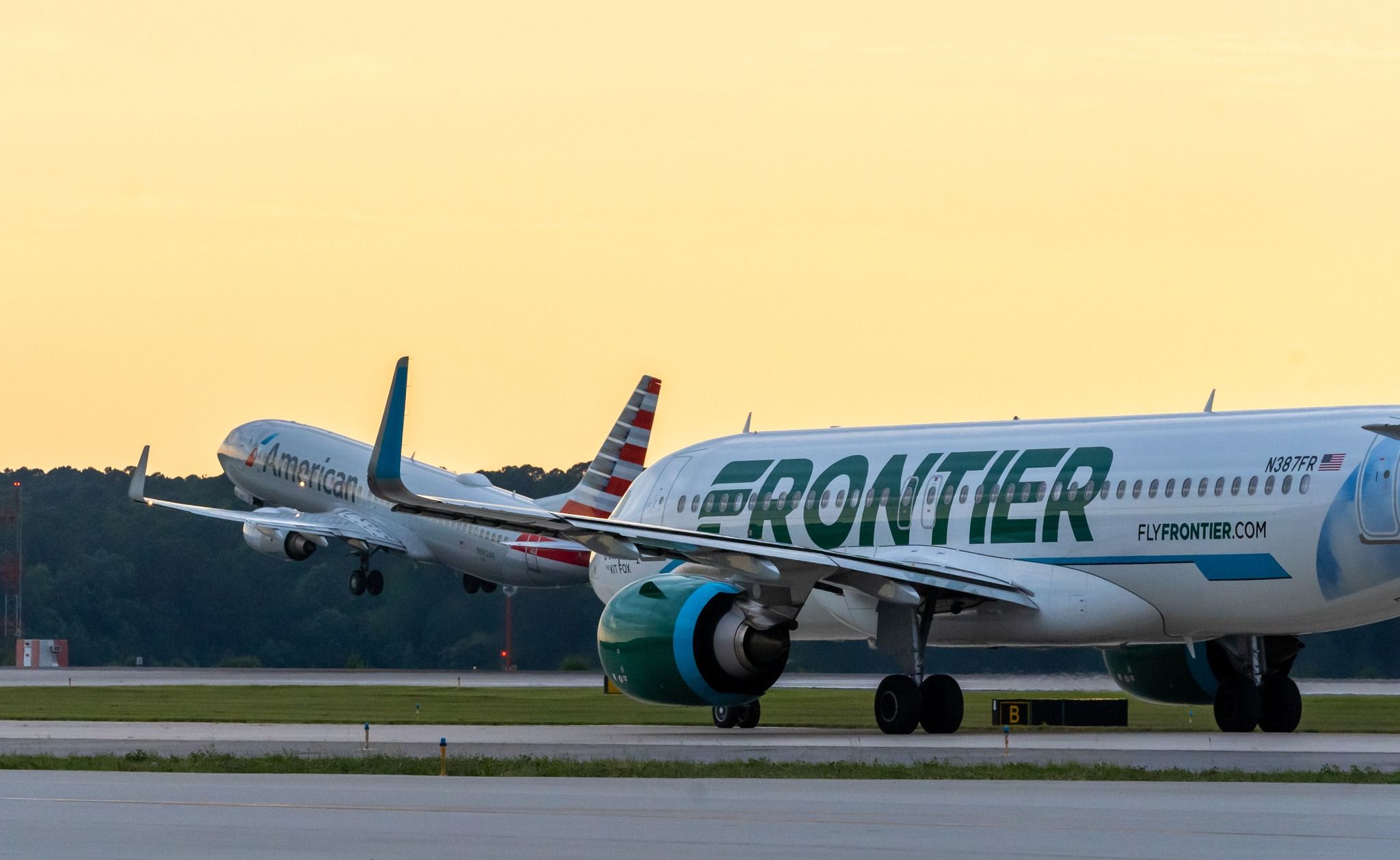 Frontier Airlines Airbus A320neo with American Airlines Boeing 737-823 taking off in the background at Raleigh-Durham International Airport.