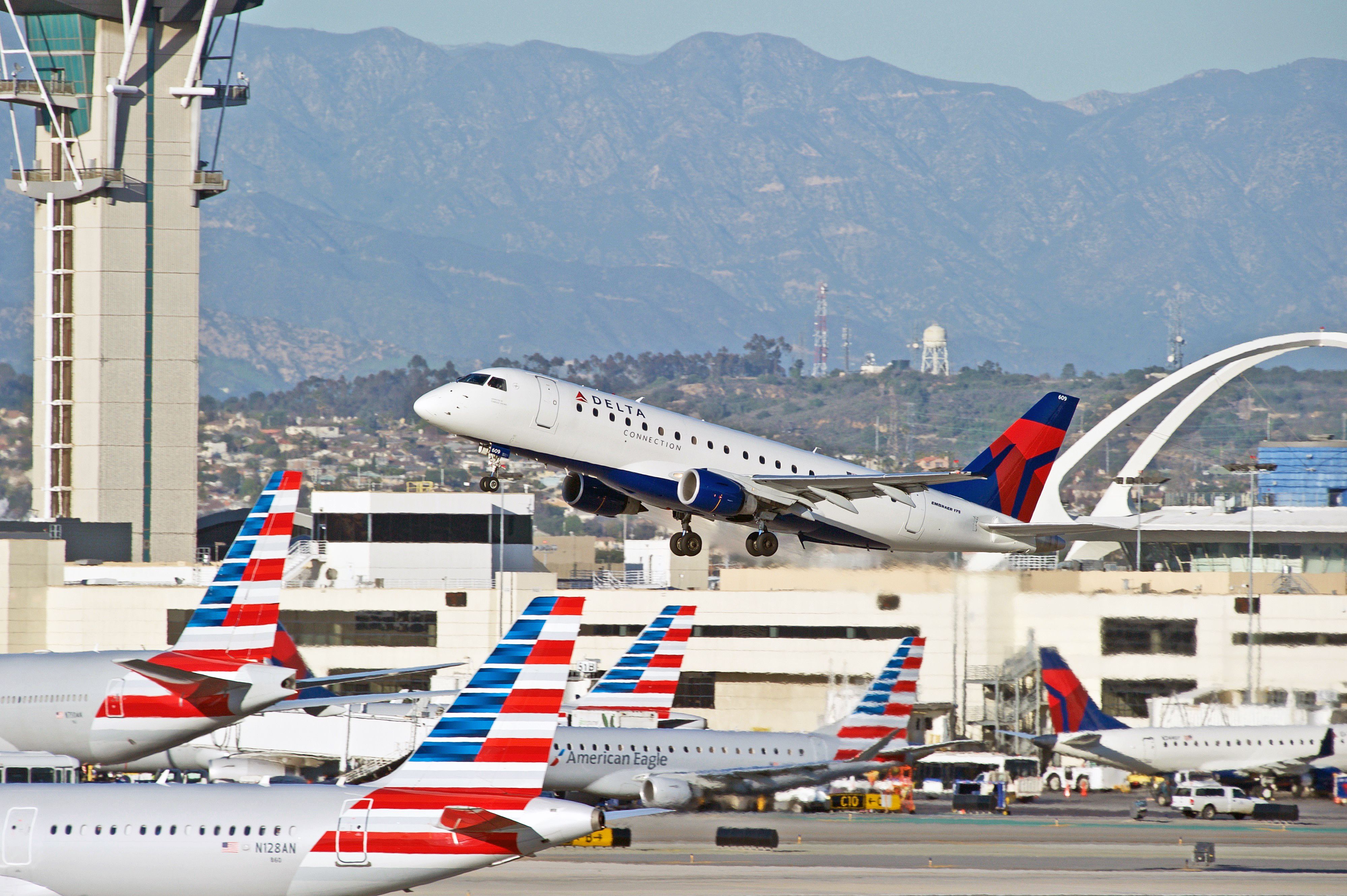 A Delta Air Lines Embraer E175 Taking Off In front of several American Airlines Planes on an airport apron.
