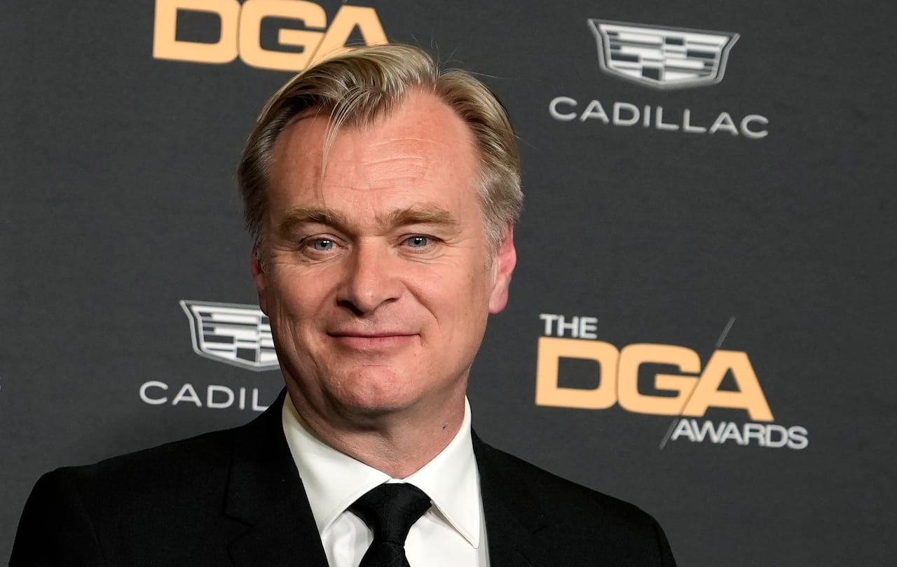 A blonde man in a black suit and tie smiles while standing in front of a wall that reads "The DGA Awards."
