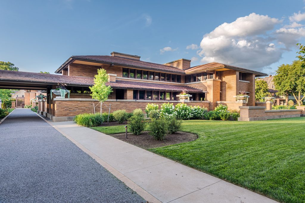 The horizontal brick Prairie-style Martin House by Frank Lloyd Wright with broad eaves and manicured lawn.