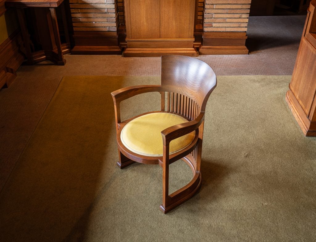 Curved wooden barrel chair with yellow cushion in warm, wood-paneled historic interior.