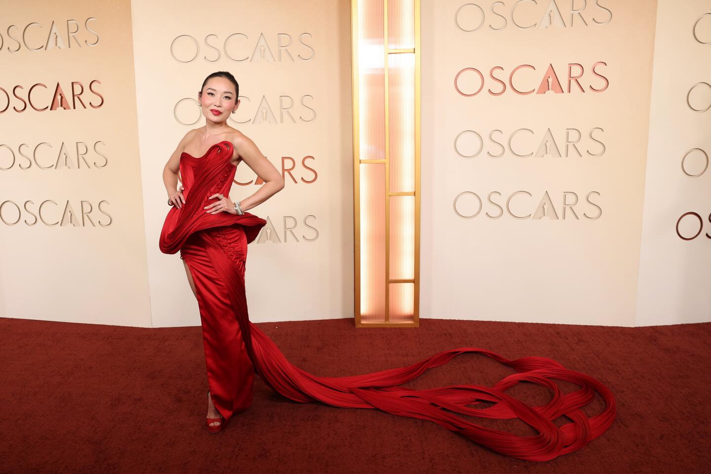 Li Jun Li, wearing a red gown with a high slit and a long train, poses on the red carpet.