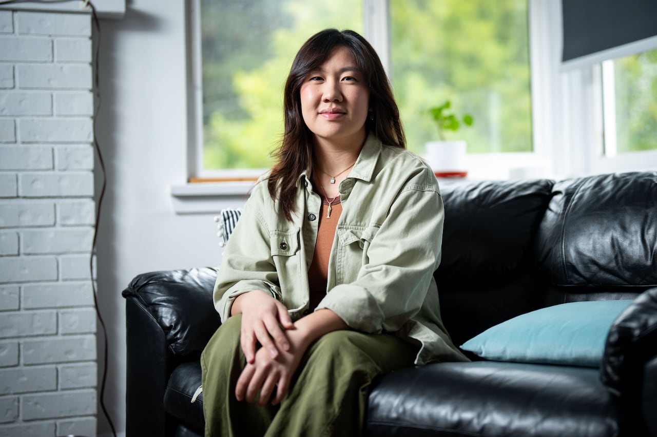 Woman with dark hair wearing green shirt and pants sits on black couch. 