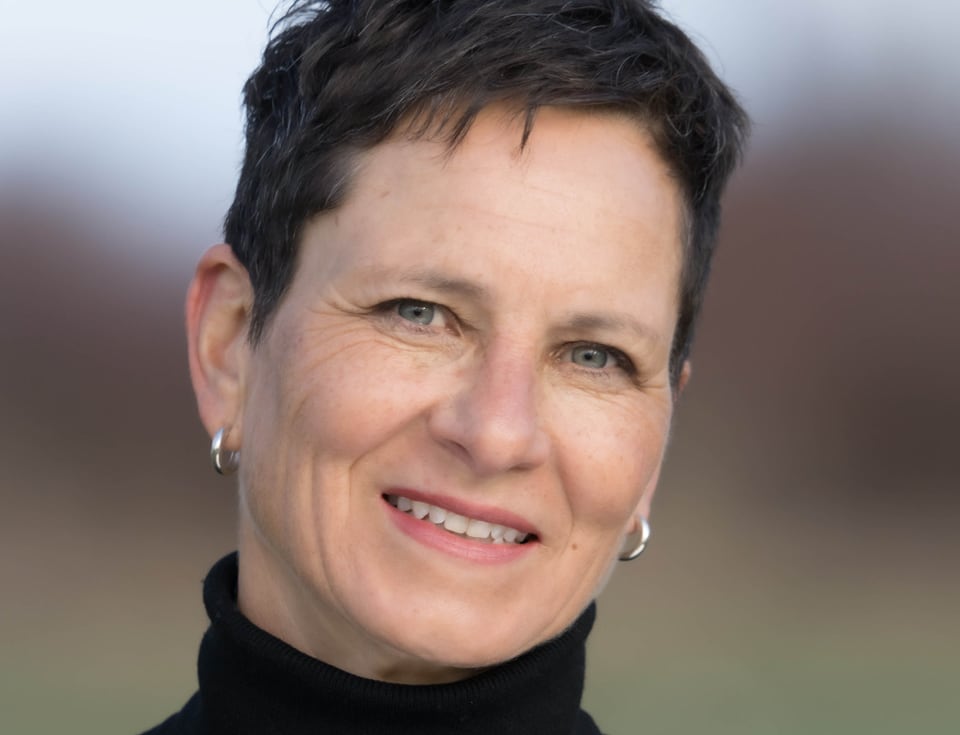 Close up of a smiling woman with short hair wearing a black turtleneck shirt and silver hoop earrings.