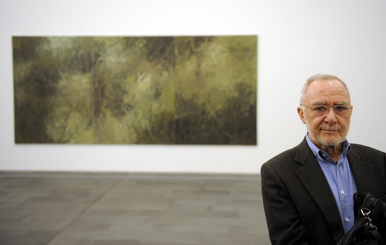 A man wearing a black blazer and blue dress shirt poses by a painting of his.