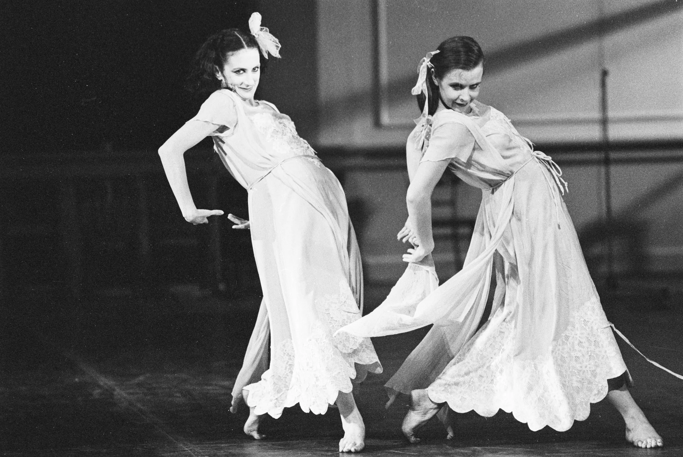 Black and white photo of two women in dresses dancing barefoot.