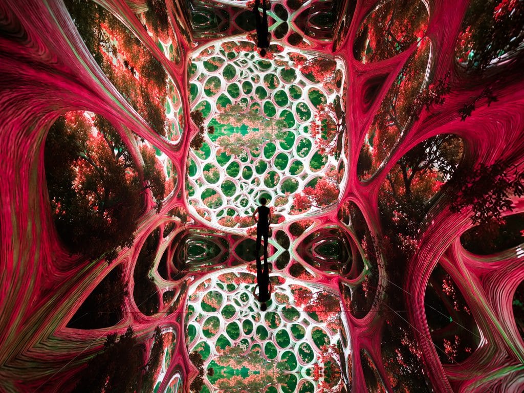 A long figure standing in an immersive space projected with visuals of organic forms