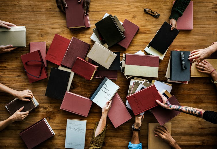People's hands reaching for a pile of old hardcover books
