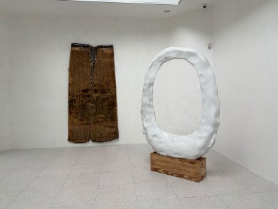 A wall-hung bronze sculpture and a white-painted free standing sculpture in a room.