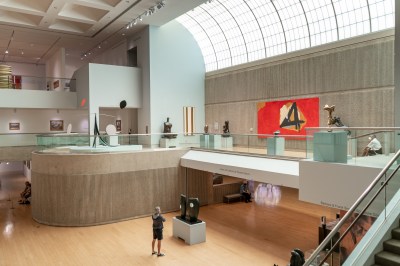 A photo shows a high-ceilinged art museum gallery with numerous modern artworks on display and skylights bringing in daylight
