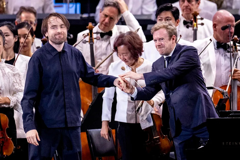 Two men on stage with an orchestra.