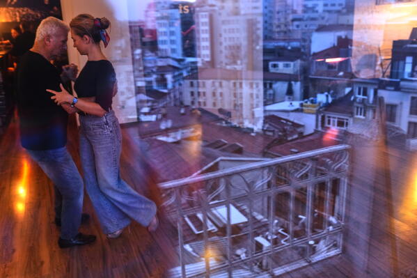 A city landscape is reflected in a window as people dance tango during a training session at 333 in Istanbul, Turkey, Sunday, Jan. 11, 2026. (AP Photo/Francisco Seco)