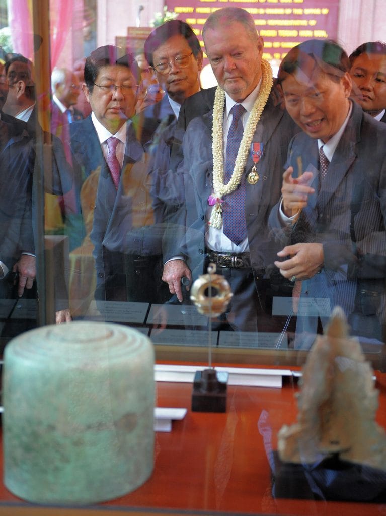 Officials and visitors examine displayed antiquities through glass cases during ceremonial event at the National Museum of Cambodia.