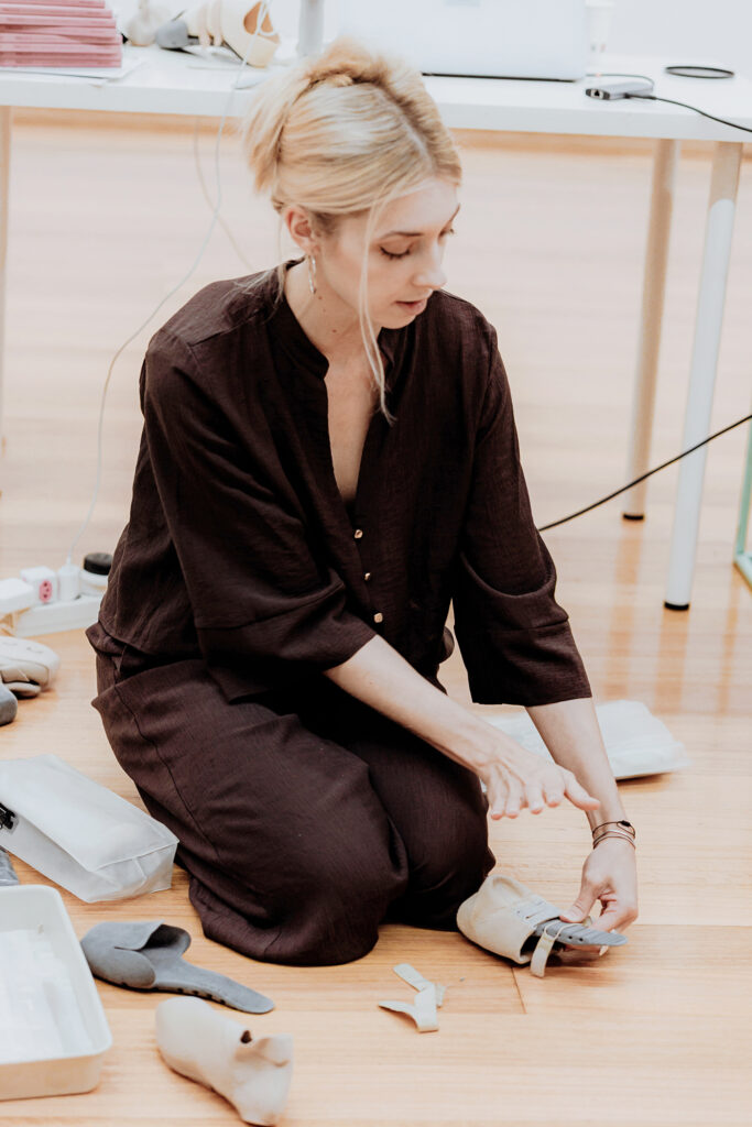 Sophia Lindner kneels on the floor while holding a 3-D printed shoe.