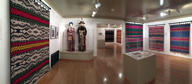 museum space with multi-colored blankets hanging on white walls