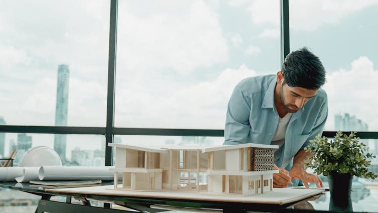 An architect making notes about his model building in front of huge glass windows.