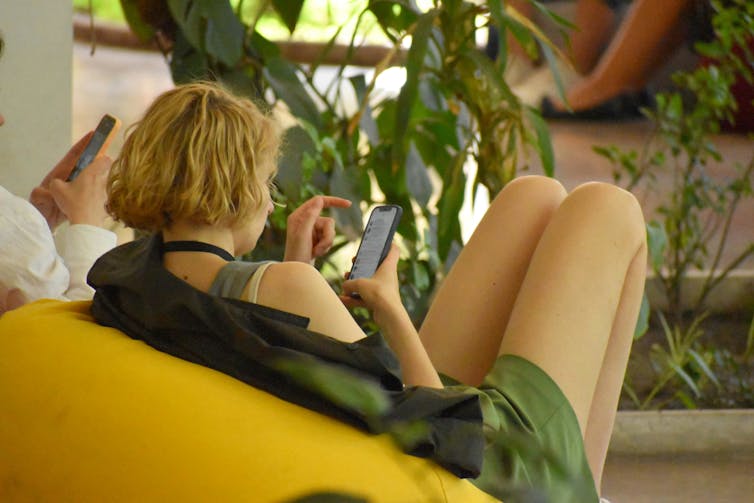 A person sitting on a chair, scrolling through their phone
