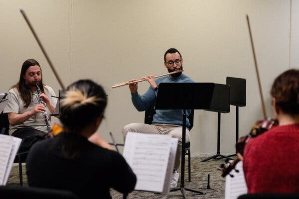 Several musicians sit while playing, arranged in a circle in a room.