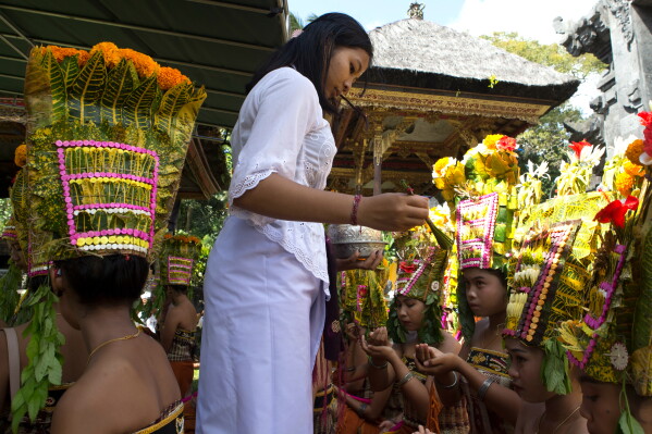 A religious volunteer, locally called "ngayah" gives blessing to dancers before performing the sacred Rejang dance during Kuningan holiday, which marks the end of the 10-day Galungan festival celebrating the victory of good over evil, in Karangasem, Bali, Indonesia, Saturday, June 27, 2026. (AP Photo/Firdia Lisnawati)