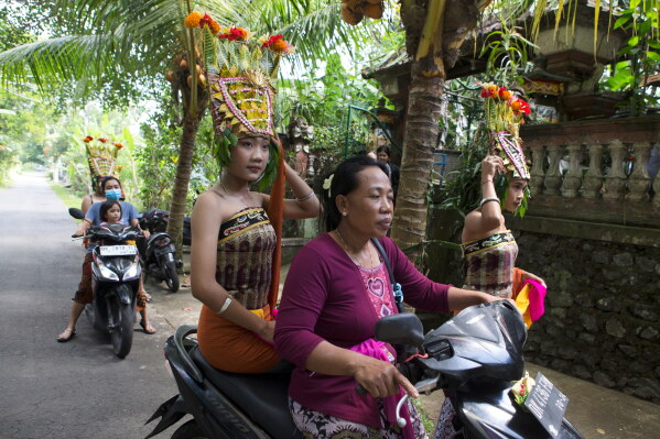 Ketut Alit Widiantary hops on a motorbike before performing the sacred Rejang dance during Kuningan holiday, which marks the end of the 10-day Galungan festival celebrating the victory of good over evil, in Karangasem, Bali, Indonesia, Saturday, June 27, 2026. (AP Photo/Firdia Lisnawati)
