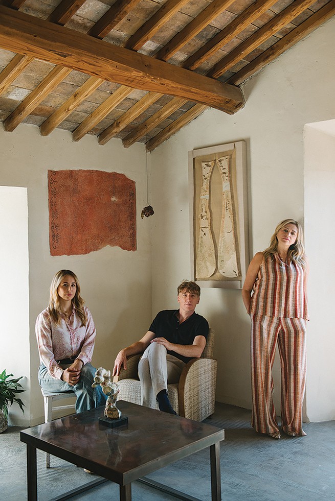 photo of woman and man sitting and woman standing in airy room with beamed ceiling