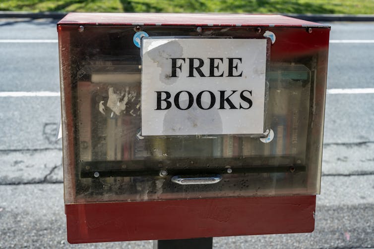 A red box with a clear case says 'free books' on the outside and has a row of books lined up inside.