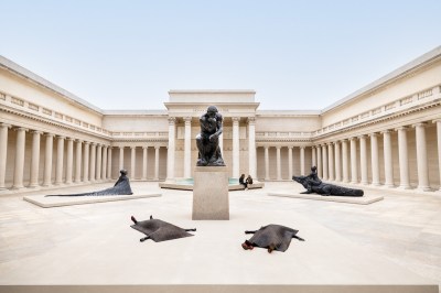 Classically styled building with columns whose atrium has a raised sculpture of a thinking man surrounded by sculptures of fantastical beings around it.