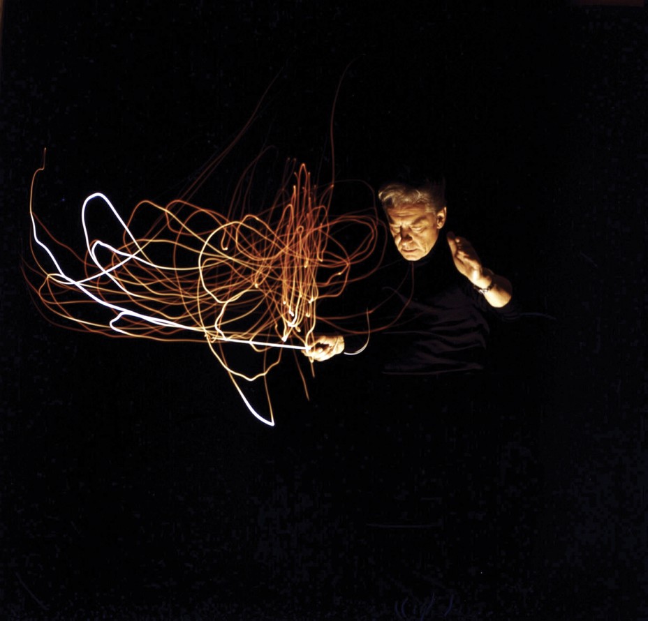 color time-lapse photo of man strongly lit from below, where the baton's movements appear as multiple tangled trails of reflected light