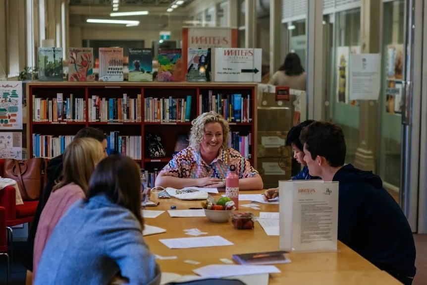 A woman, Danielle Binks, talks to a group of school students in a library