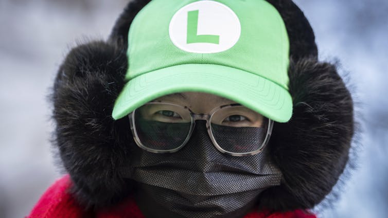 A supporter outside court wears eyeglasses, a black face mask and a green hat with an 'L' logo