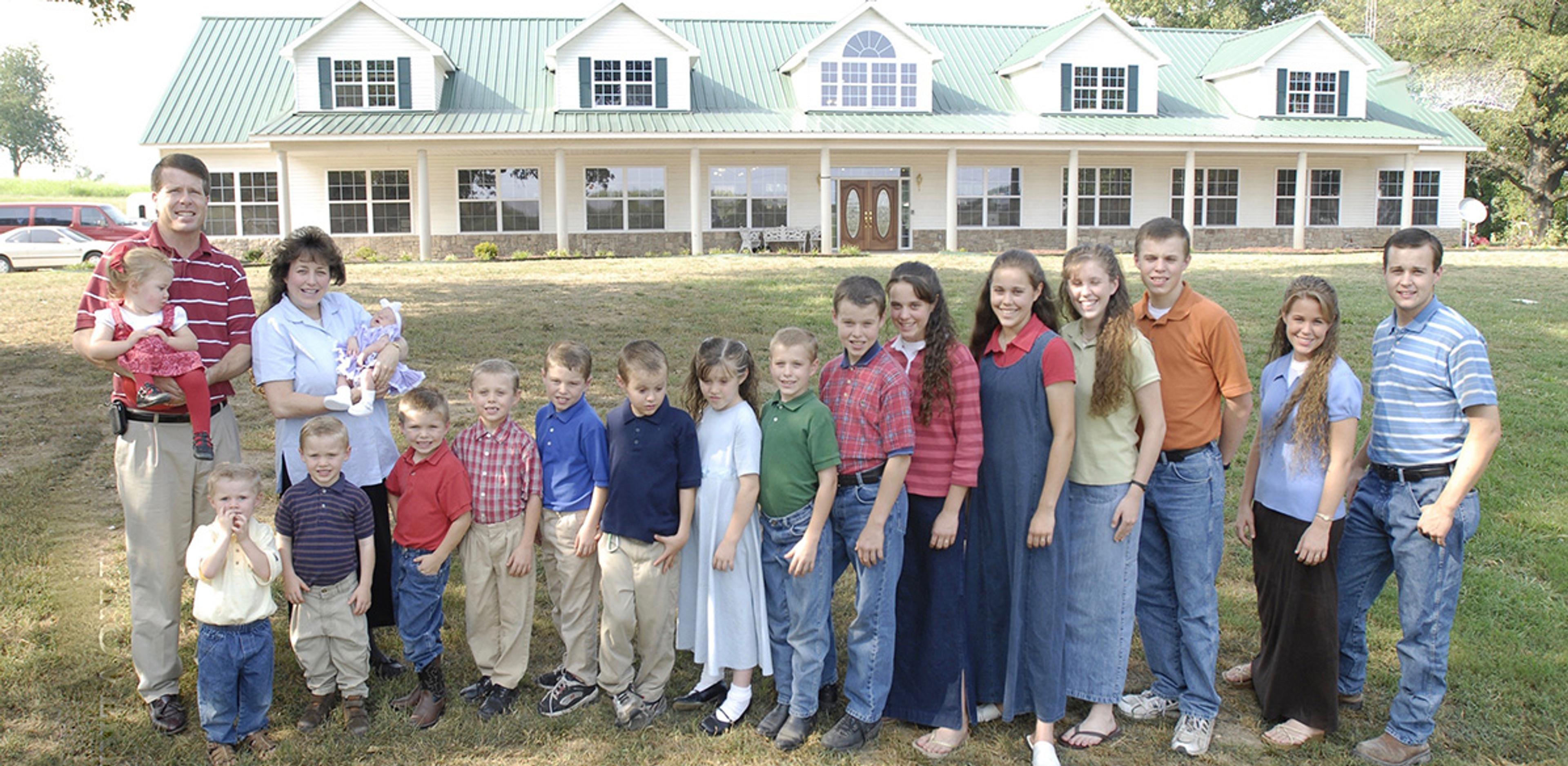 A large family poses in front of a house with a green roof and dormer windows in this photo.