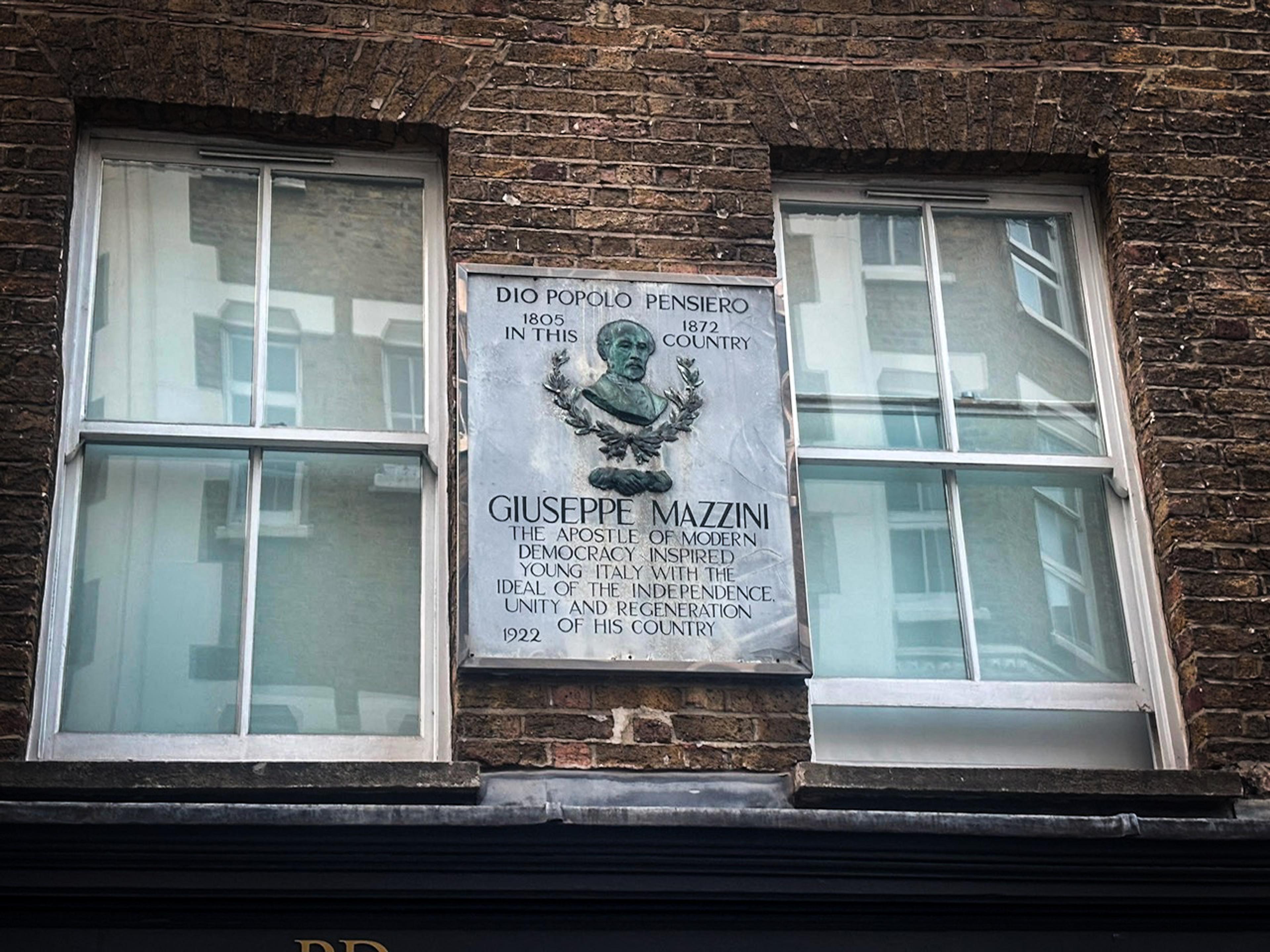 Giuseppe Mazzini plaque between two windows on a brick building, commemorating him as an apostle of democracy.