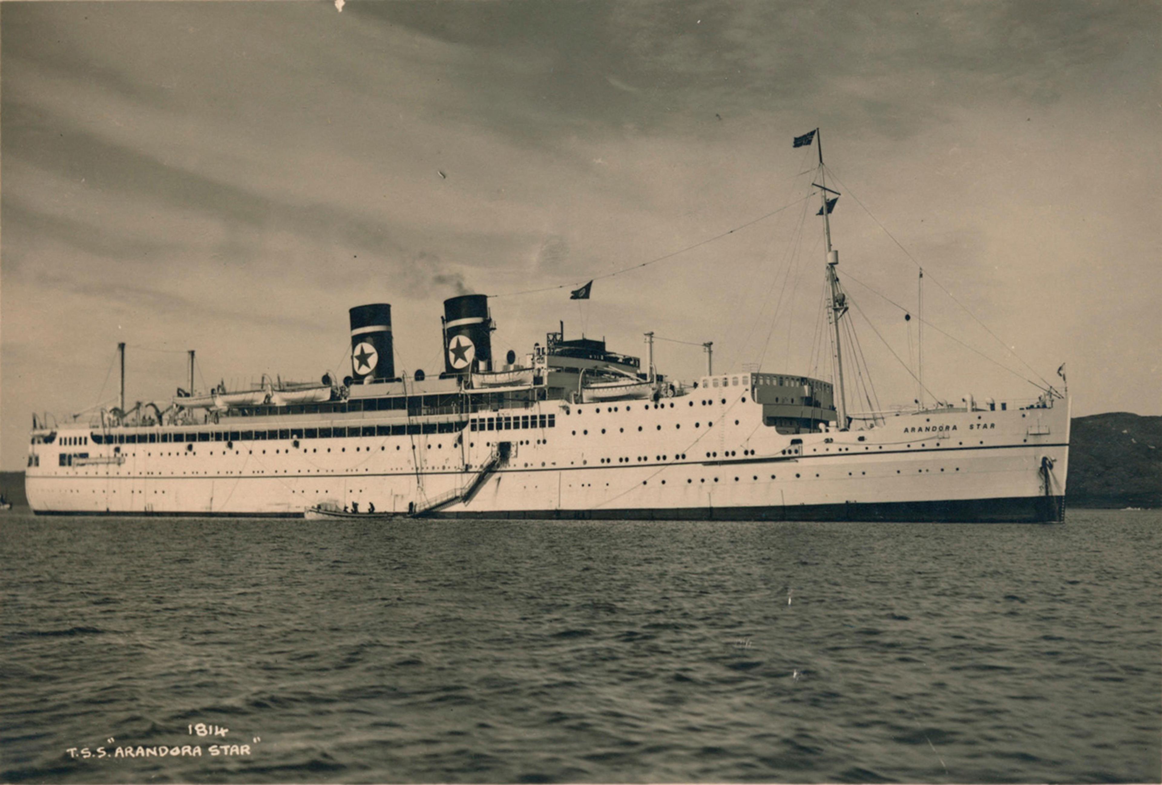 Vintage photo of the ocean liner T.S.S. Arandora Star with two funnels and a star emblem, anchored in calm water.