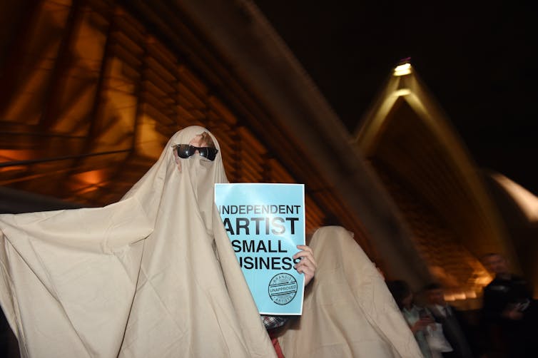 Someone in a ghost costume, holding a sign saying 'independent artist, small business'.