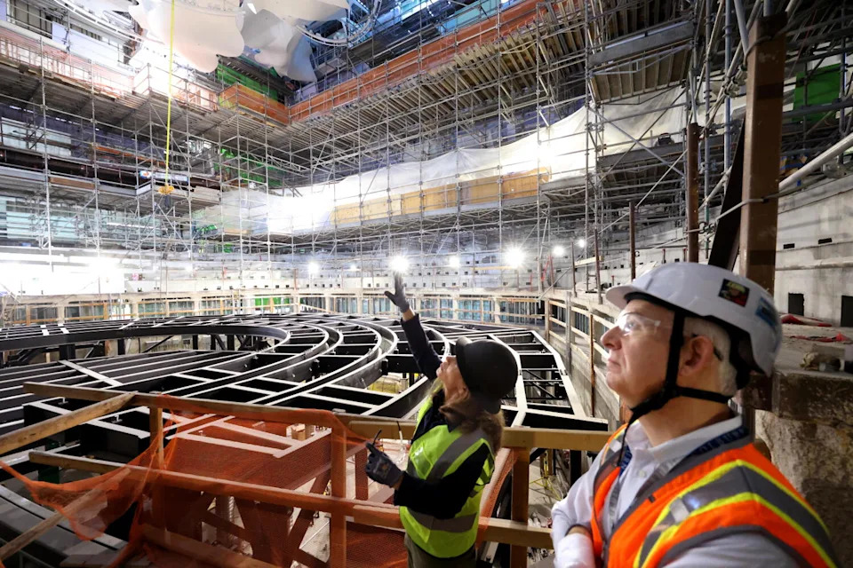 Two people in hard hats look at a concert hall under construction.