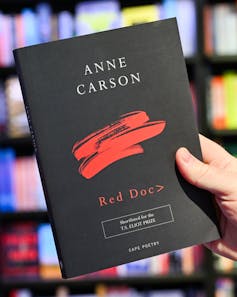 A hand holding a black book with red lettering.